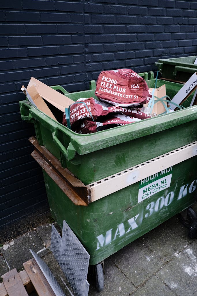 Urban scene of a green dumpster filled with cardboard waste for recycling.